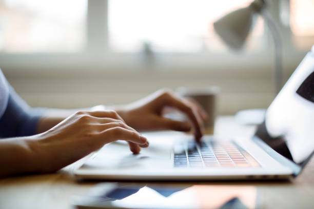Hands typing on a laptop keyboard at a desk with a mug and blurred background.
