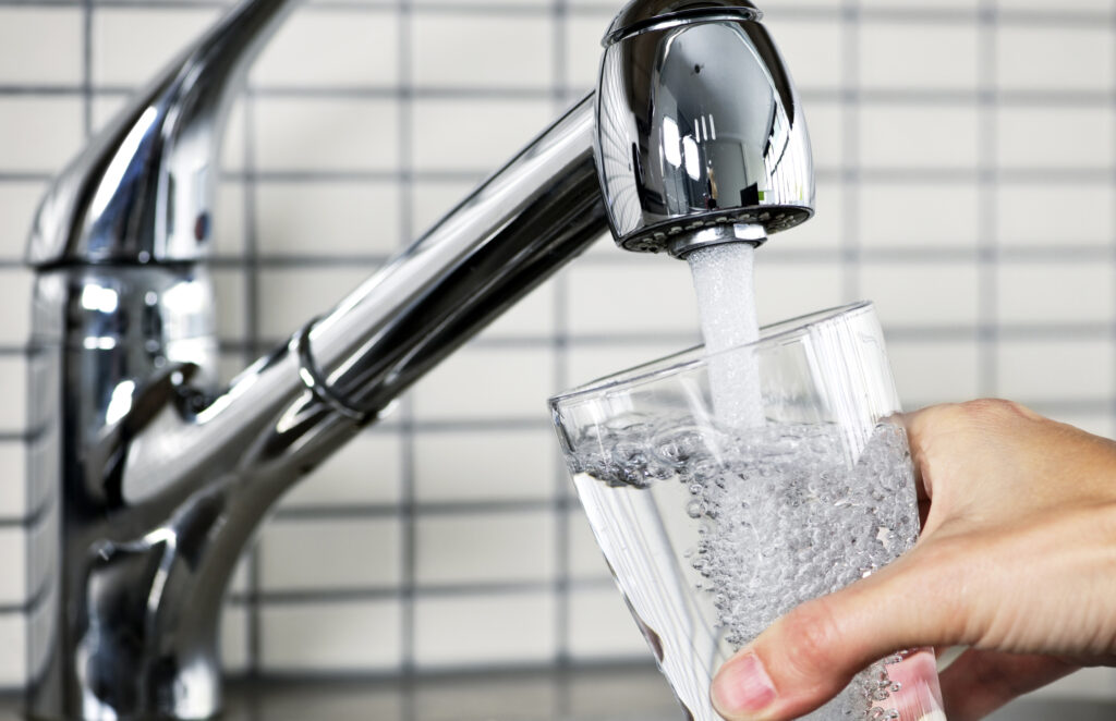 A hand holds a glass under a stream of water from a modern chrome faucet.