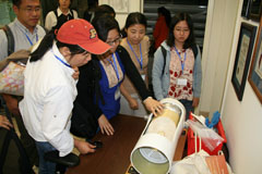 Group of people gathered around a white cylindrical device on a table during a demonstration.