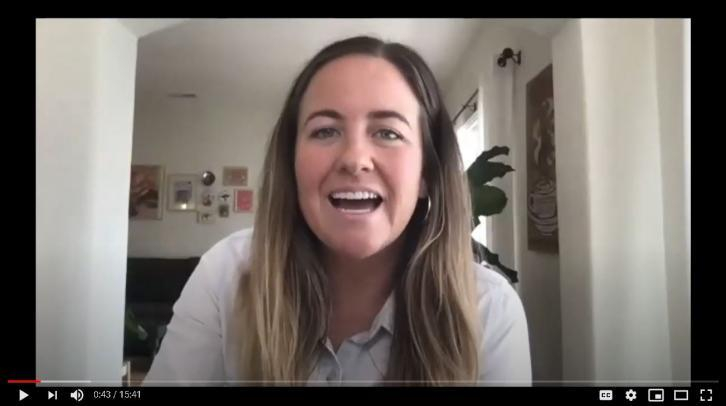 Smiling woman with long hair speaks in a video call, in a bright home office with plants and wall art.