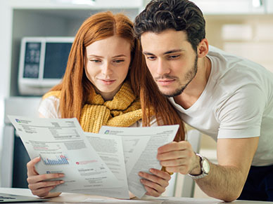 Two professionals, a man and a woman, examine financial documents with charts at a desk.