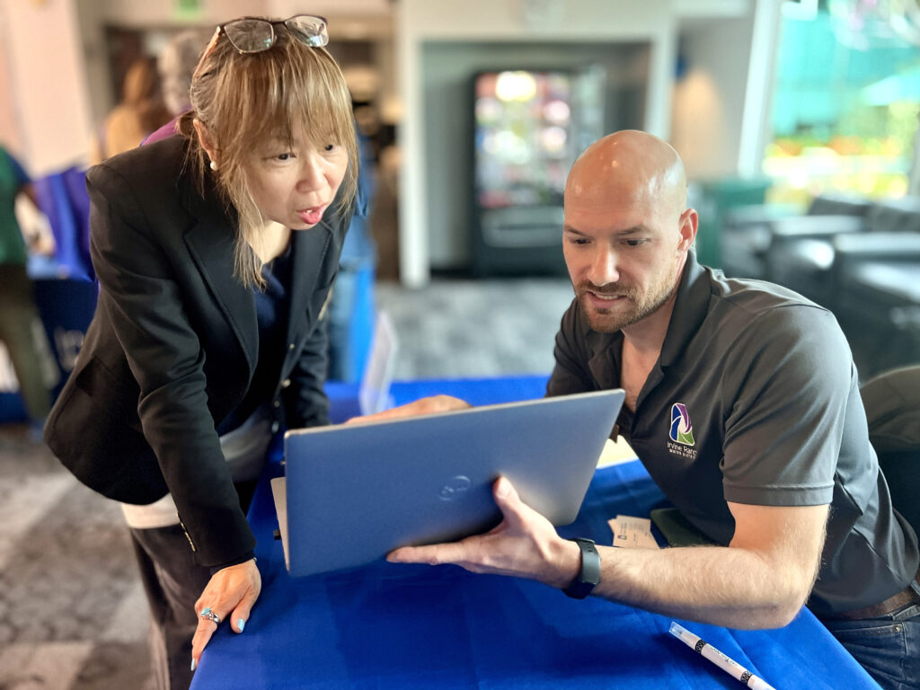 Two colleagues review a blue laptop screen at a table covered with a blue cloth.