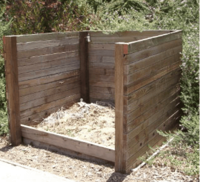 Raised wooden compost bin with soil inside in a garden